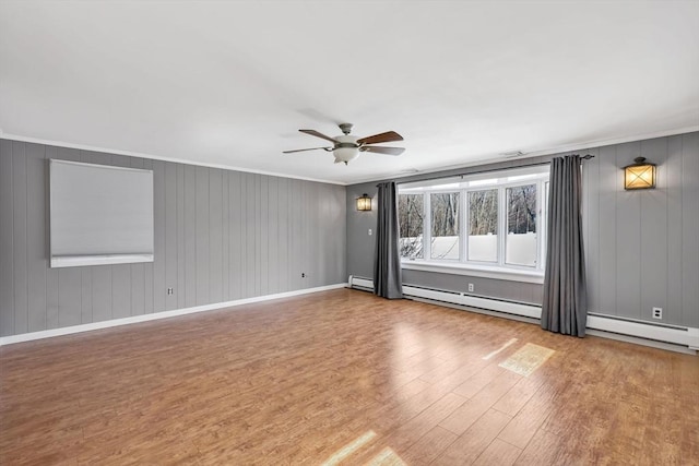 unfurnished room with wood finished floors, baseboards, ceiling fan, ornamental molding, and a baseboard heating unit