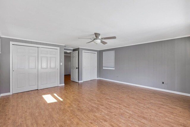 unfurnished bedroom featuring light wood-style flooring, baseboards, two closets, and ornamental molding