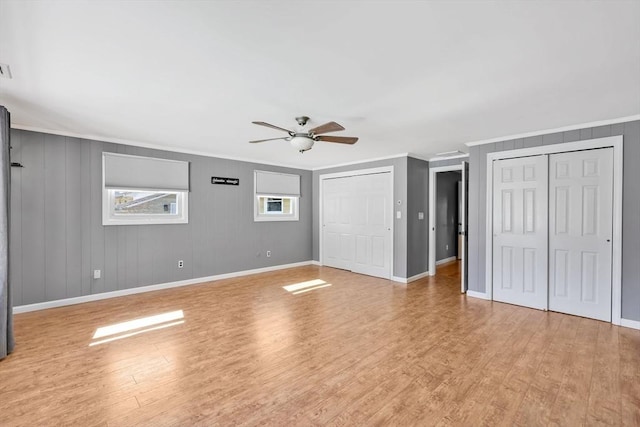 interior space with a ceiling fan, baseboards, light wood-style flooring, ornamental molding, and multiple closets