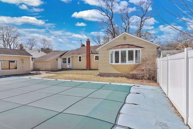 rear view of property featuring a fenced in pool, a chimney, and fence