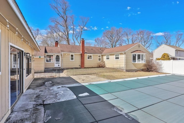 rear view of property featuring a patio area, fence, a fenced in pool, and a chimney