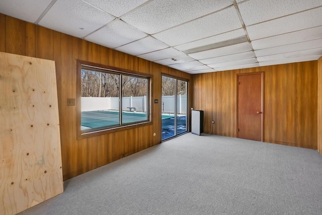 carpeted spare room with a paneled ceiling and wood walls