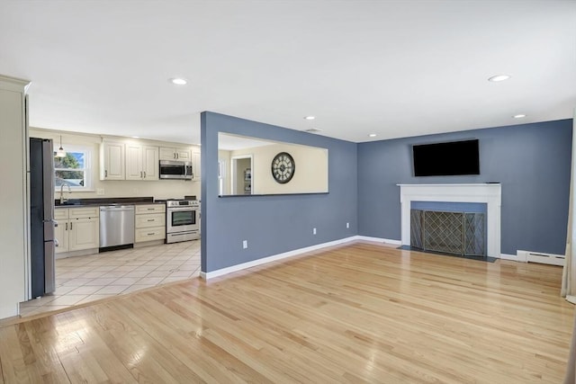 unfurnished living room featuring baseboards, light wood finished floors, a baseboard radiator, a fireplace with flush hearth, and a sink