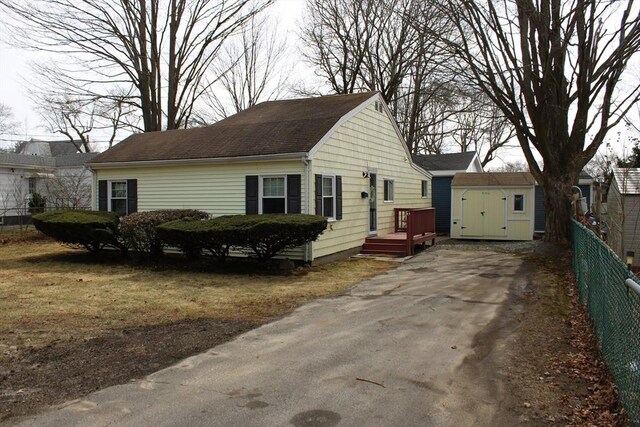 view of front of property with a storage unit, an outbuilding, aphalt driveway, and fence