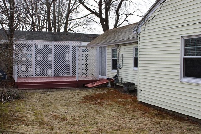 view of side of home featuring a lawn, a shingled roof, and a deck