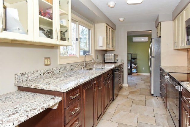 kitchen with cream cabinets, an AC wall unit, sink, appliances with stainless steel finishes, and light stone counters