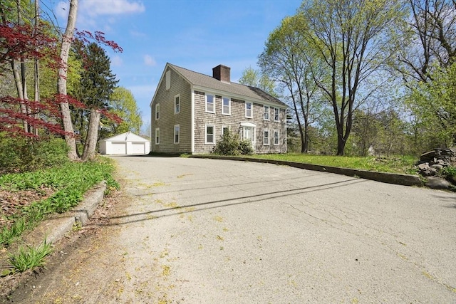 colonial inspired home featuring an outbuilding, a chimney, and a garage