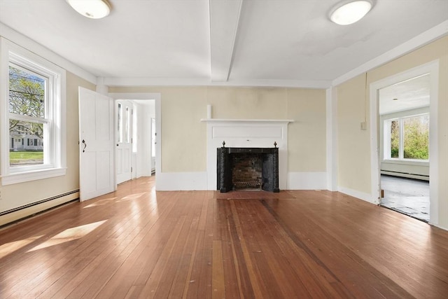 unfurnished living room with a fireplace with flush hearth, baseboard heating, hardwood / wood-style flooring, and a wealth of natural light