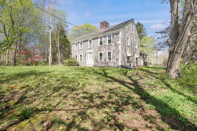 rear view of property featuring a chimney and a yard