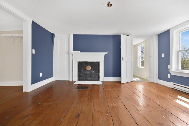 unfurnished living room featuring baseboards, visible vents, a fireplace with flush hearth, and hardwood / wood-style floors