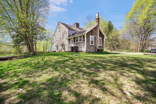 view of side of property featuring a lawn, a chimney, and roof with shingles