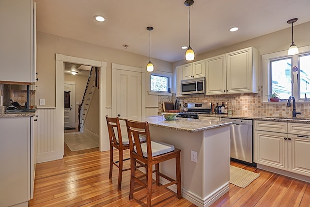 kitchen featuring white cabinets, sink, appliances with stainless steel finishes, a kitchen island, and light stone counters