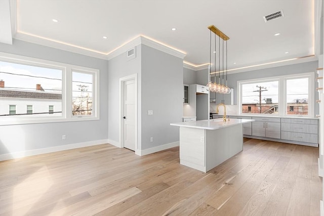 308 Newton St, Waltham, MA 02453 - kitchen with light wood-type flooring, light countertops, a kitchen island with sink, baseboards, and hanging light fixtures