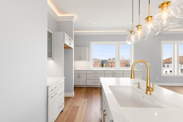 308 Newton St, Waltham, MA 02453 - kitchen featuring a sink, light wood-style flooring, pendant lighting, glass insert cabinets, and ornamental molding