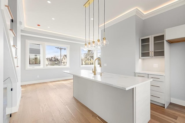 308 Newton St, Waltham, MA 02453 - kitchen with light wood-style flooring, baseboards, a kitchen island with sink, glass insert cabinets, and ornamental molding