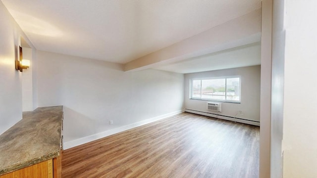 unfurnished room with light wood-style floors, baseboards, a wall unit AC, and a baseboard heating unit