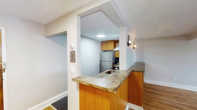 kitchen featuring freestanding refrigerator, a peninsula, baseboards, and brown cabinetry