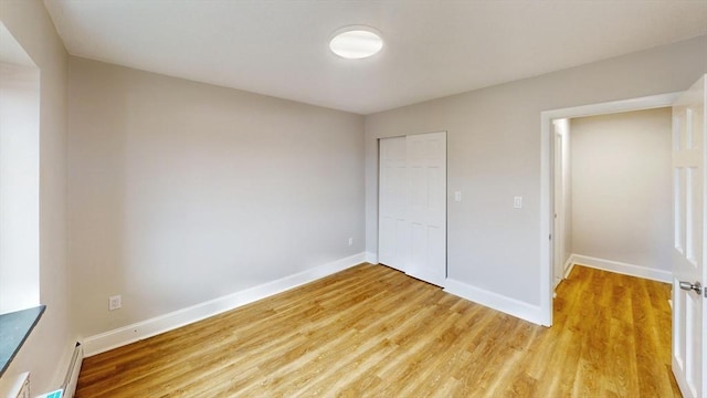 unfurnished bedroom with light wood-style flooring, baseboards, a closet, and baseboard heating