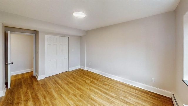 unfurnished bedroom with light wood finished floors, baseboards, and a baseboard radiator