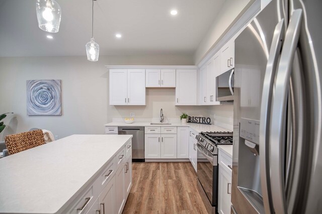 kitchen featuring white cabinetry, sink, pendant lighting, appliances with stainless steel finishes, and light wood-type flooring