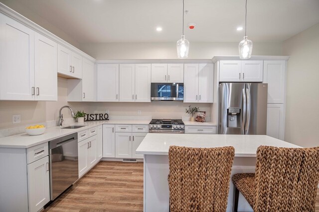 kitchen featuring hanging light fixtures, sink, light hardwood / wood-style flooring, appliances with stainless steel finishes, and white cabinetry