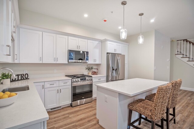 kitchen featuring appliances with stainless steel finishes, white cabinetry, a kitchen island, and sink