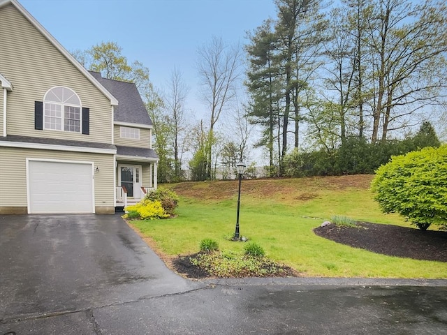 view of green lawn with a garage and asphalt driveway