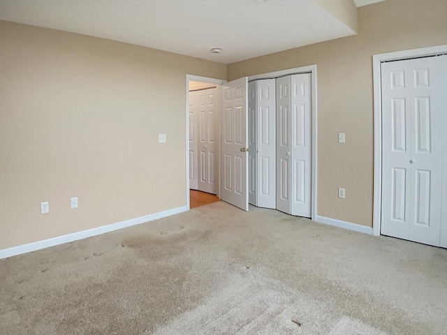 unfurnished bedroom featuring two closets, carpet, and baseboards