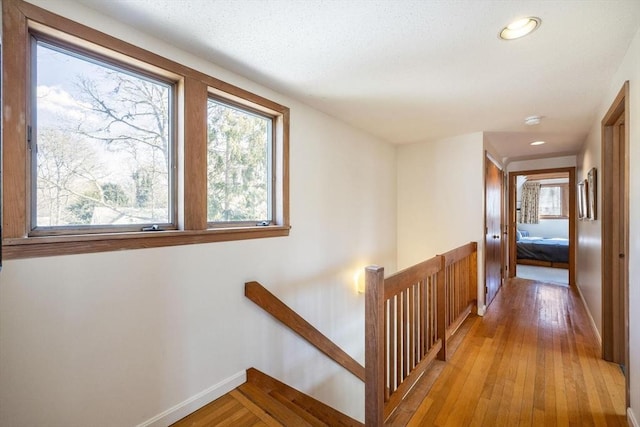 hallway featuring recessed lighting, light wood-type flooring, an upstairs landing, and baseboards