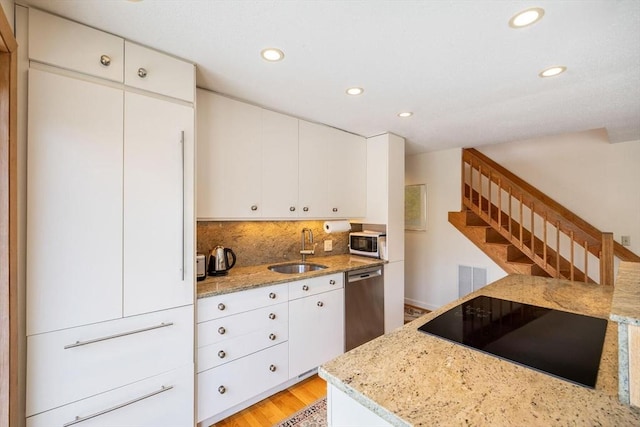 kitchen featuring light stone counters, a sink, dishwasher, black electric cooktop, and backsplash