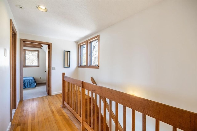 hallway with an upstairs landing, a healthy amount of sunlight, light wood-style flooring, and baseboards