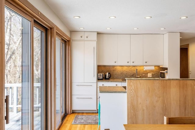 kitchen with light stone countertops, decorative backsplash, recessed lighting, light wood-style flooring, and white cabinetry