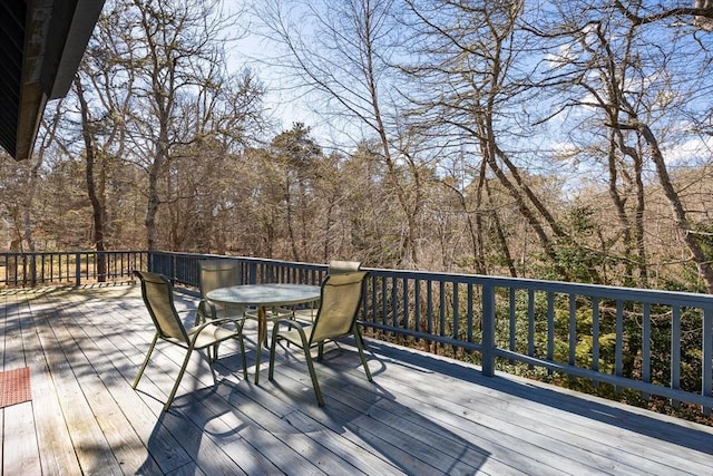 wooden terrace with a view of trees and outdoor dining area