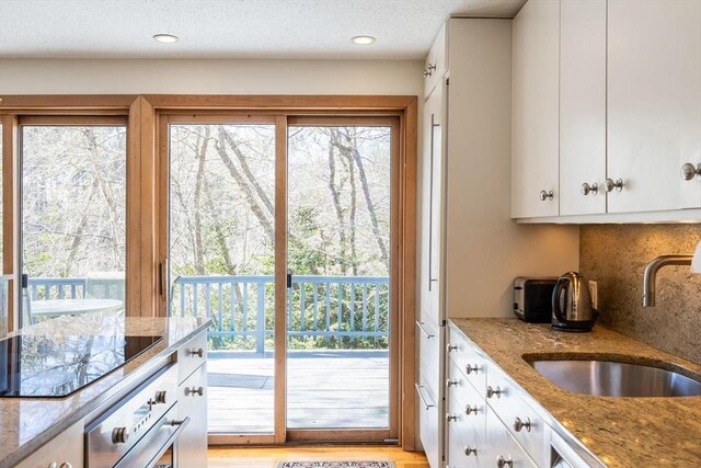 kitchen featuring oven, a sink, tasteful backsplash, white cabinets, and black electric stovetop