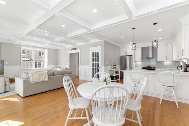 dining area with light wood-type flooring, beam ceiling, coffered ceiling, and a wainscoted wall