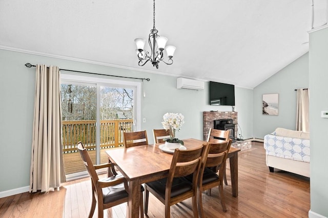dining room with a notable chandelier, a wall mounted air conditioner, a fireplace with raised hearth, vaulted ceiling, and light wood-style floors