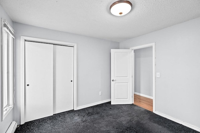 unfurnished bedroom with a baseboard radiator, a closet, a textured ceiling, baseboards, and dark colored carpet