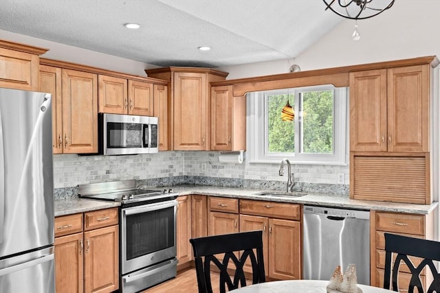kitchen with a sink, decorative backsplash, light stone counters, and appliances with stainless steel finishes