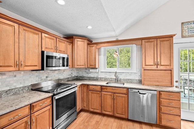 kitchen featuring light wood-type flooring, stainless steel appliances, brown cabinetry, and a sink
