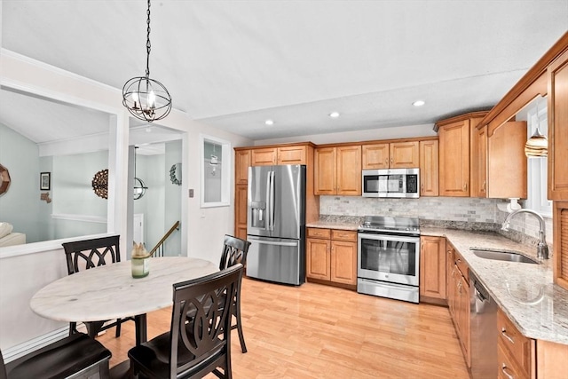 kitchen with a sink, stainless steel appliances, light wood-type flooring, light stone counters, and backsplash