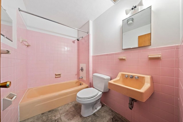 full bathroom featuring toilet, a sink, shower / bath combination, tile walls, and wainscoting