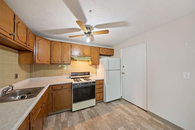 kitchen with light wood finished floors, a sink, freestanding refrigerator, range with gas cooktop, and under cabinet range hood