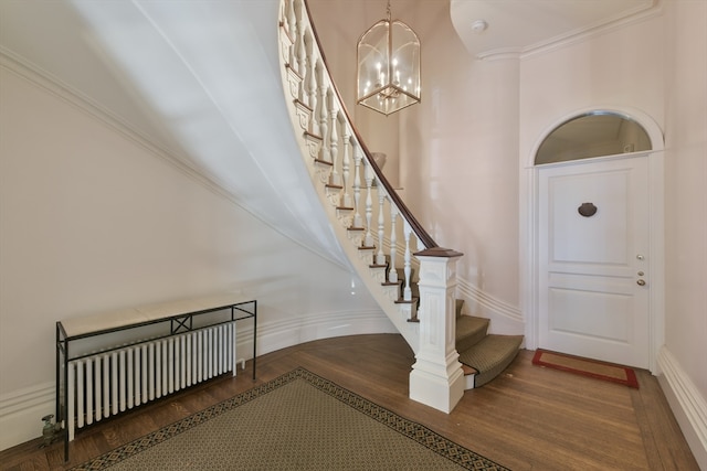 entrance foyer featuring a notable chandelier, radiator heating unit, crown molding, and hardwood / wood-style floors