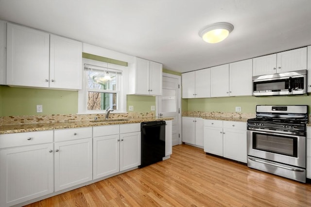 kitchen with light wood-type flooring, appliances with stainless steel finishes, white cabinets, and a sink