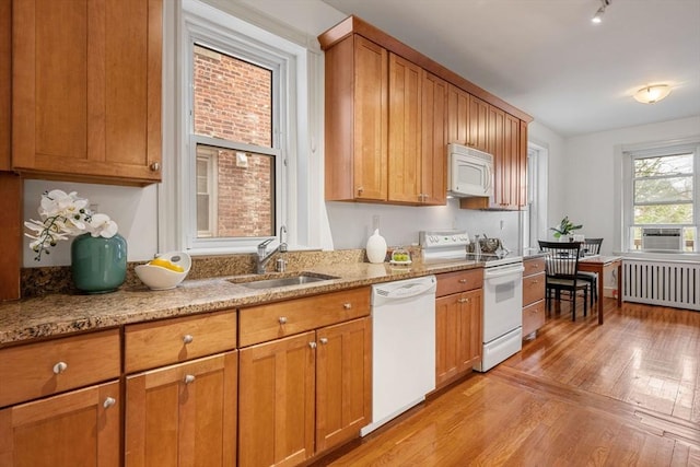 kitchen featuring radiator, a sink, light wood-style floors, brown cabinetry, and white appliances