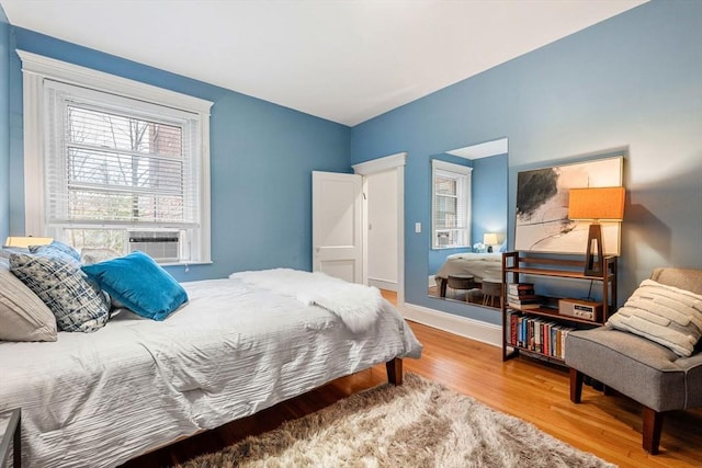 bedroom with cooling unit, wood finished floors, and baseboards