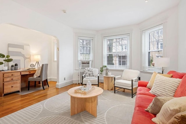 sitting room featuring wood finished floors, plenty of natural light, arched walkways, and baseboards