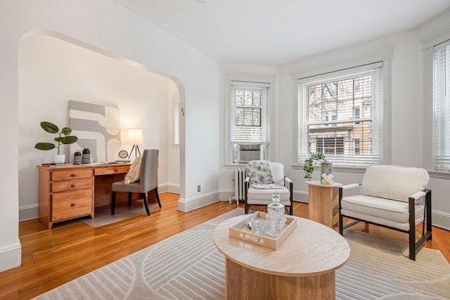 living area with cooling unit, light wood finished floors, arched walkways, and baseboards