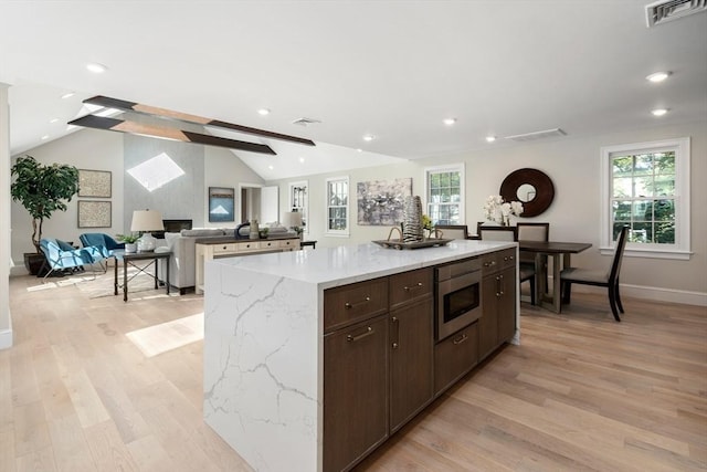 kitchen featuring stainless steel microwave, vaulted ceiling, light wood-type flooring, a kitchen island, and baseboards