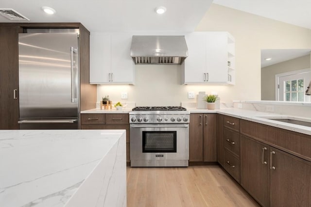 kitchen with premium appliances, ventilation hood, white cabinets, light wood finished floors, and recessed lighting